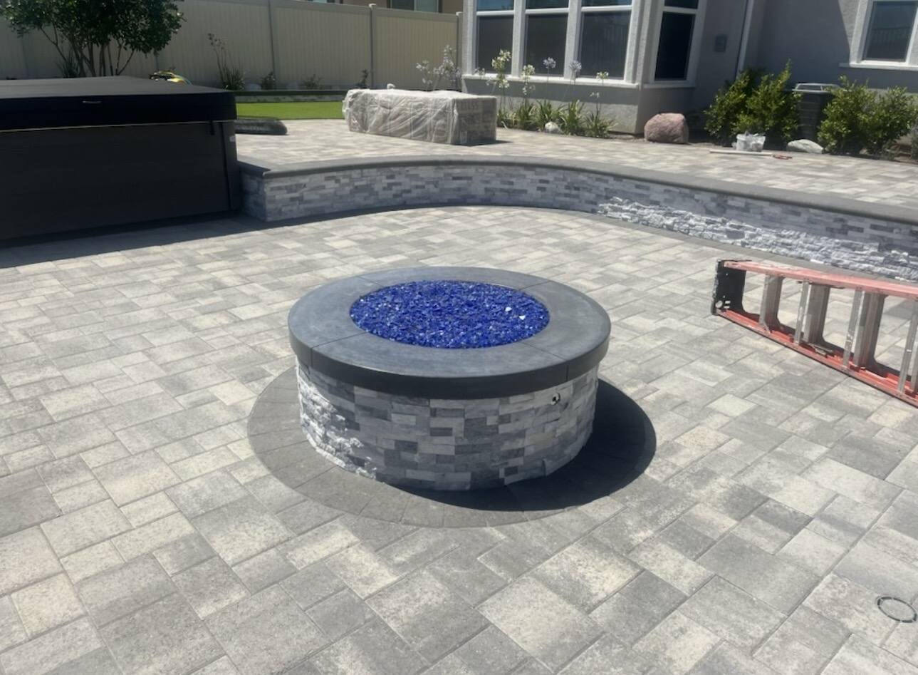 Paver patio with a round stone clad gas fire pit filled with blue fire glass, and a raised seat wall behind
